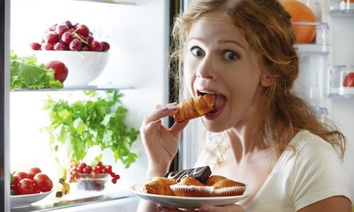 woman eats sweets at night to sneak in a refrigerator