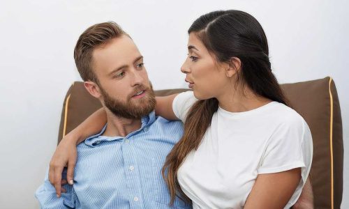 Happy young couple, Caucasian man and Latin-American woman, communicating when sitting together cuddling on coach