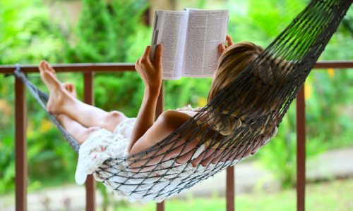 8581034 - young woman reading a book lying in a hammock