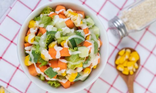 Cucumber salad, corn, carrot and lettuce in a white cup. top view.