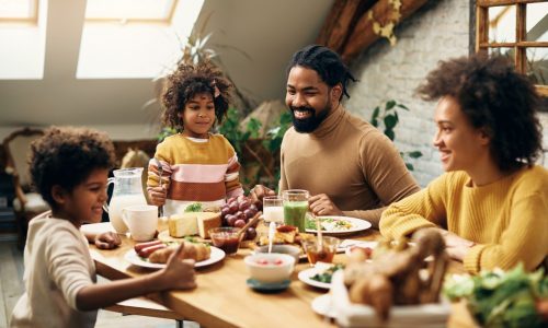 Happy African American parents and their kids enjoying in family meal at dining table.