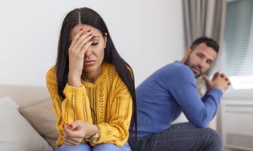 Sad pensive young girl thinking of relationships problems sitting on sofa with offended boyfriend, conflicts in marriage