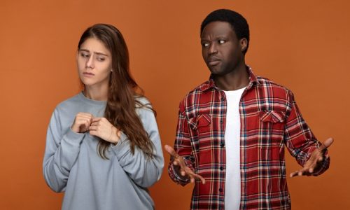 Clueless young guy of African ethnicity being at lost, looking at his girlfriend with confused facial expression, can't understand her at all. Uncertain white woman feeling unhappy with her boyfriend