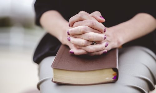 A woman  sitting with hand together on a book on her lap